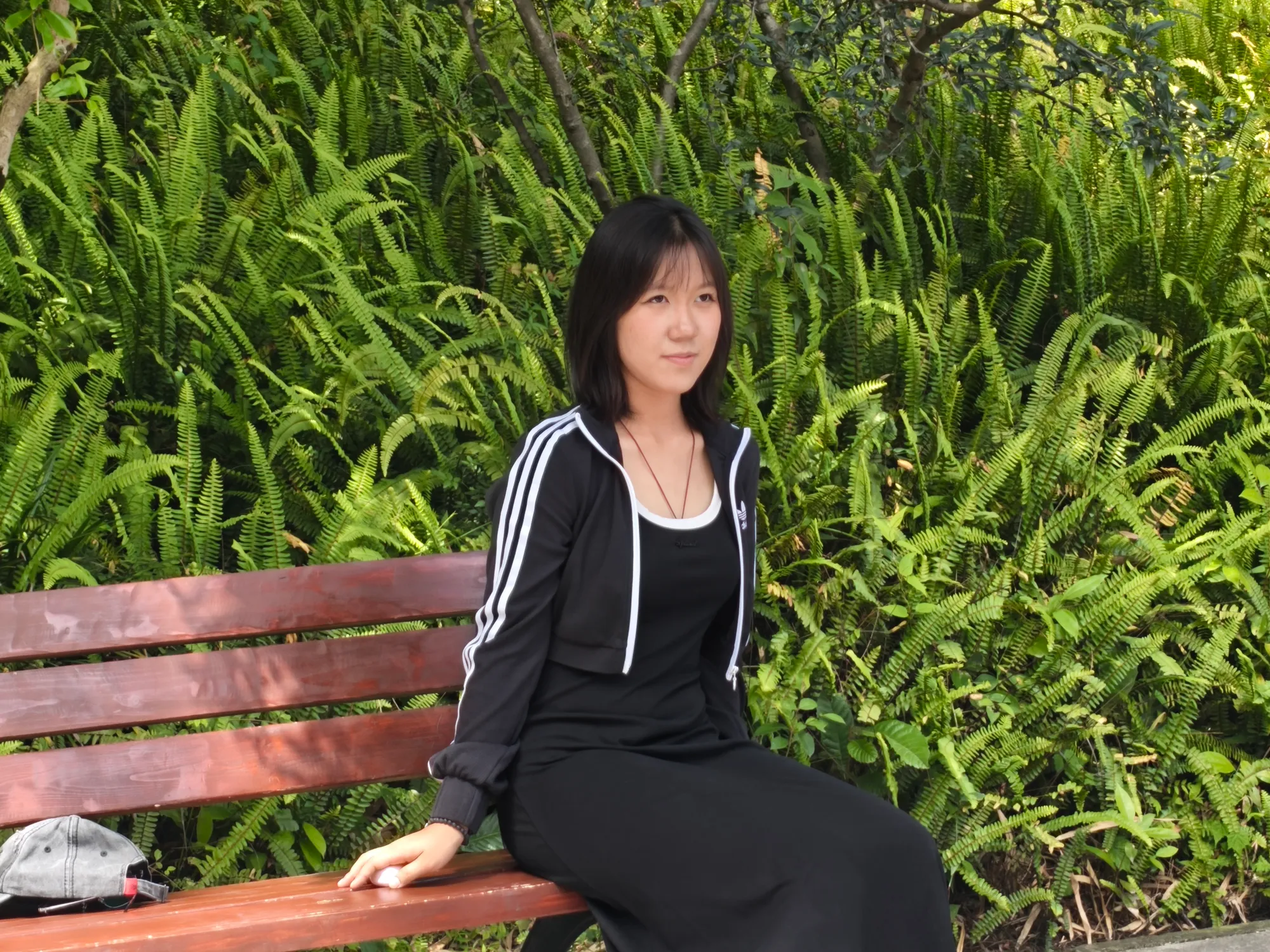 一位女同学坐在一条凳子上,背景里是绿色的草丛