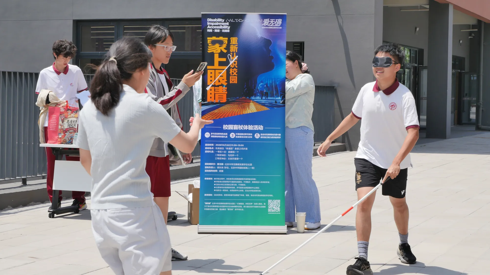 一位志愿者引导一位蒙着眼睛的学生使用盲杖导览校园